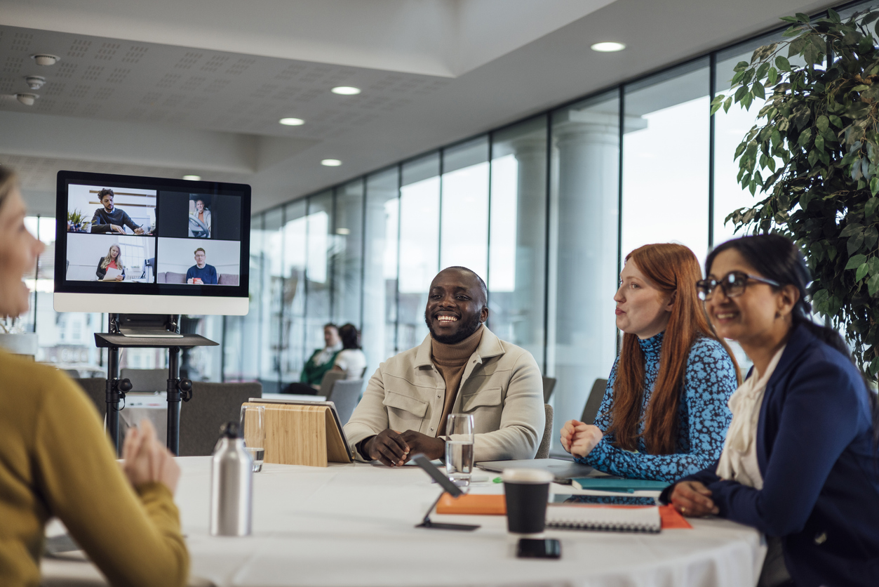 4 people working together in a modern office with a screen behind, highlighting Ideal's Smart Future-Proof Workplace solutions.